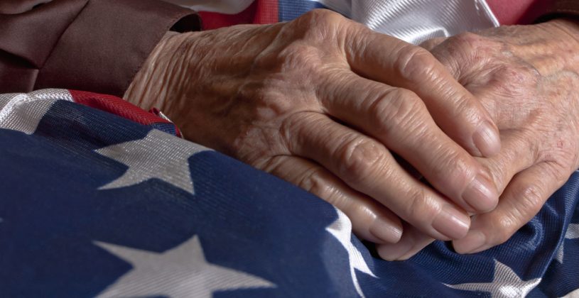 Elderly man's hands resting on the American flag. Lighthouse Senior Living honors Veteran's Day