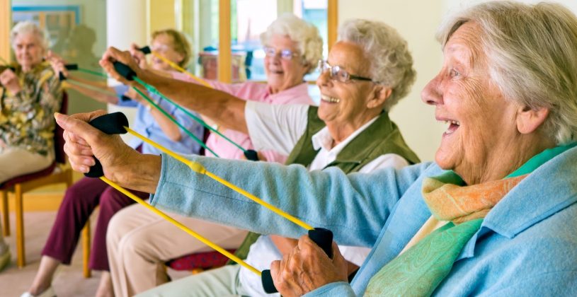 Senior women sitting in chairs and enjoying a low-impact exercise class with bands