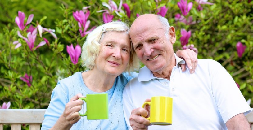 Senior couple drinking coffee on a garden bench in spring. Finding ways to address seasonal allergies will help you enjoy the spring season.