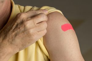 Bandaid on arm of senior man. The CDC recommends that all healthy adults 50 and older receive the shingles vaccine.