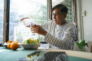 Senior man sitting at kitchen table pouring a glass of water