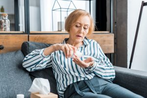 Image of a senior woman sitting on a couch emptying medication into her hand.
