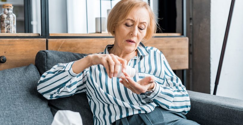 Image of a senior woman sitting on a couch emptying medication into her hand.