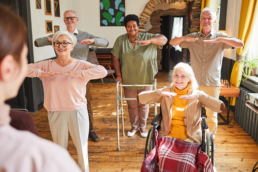 Diverse group of smiling senior people enjoying morning exercises in retirement home, copy space