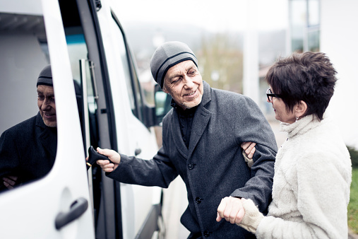 Caregiver helping senior man enter a van
