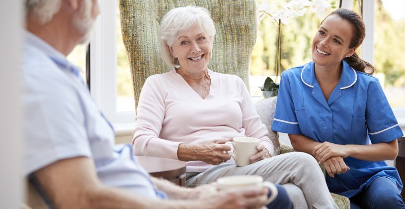 Senior couple sitting and talking with a caregiver at an Assisted Living facility.