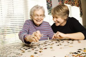 Image of a happy senior woman doing a puzzle with a friend.