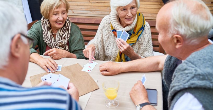 four seniors sitting around a table playing a card game together
