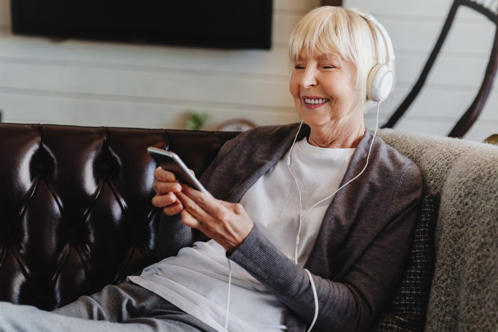 senior woman wearing headphones and smiling while listening to one of the best podcasts for seniors
