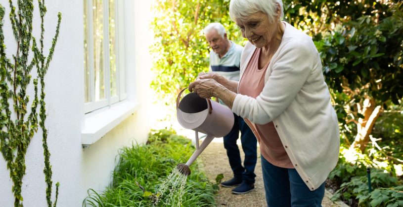 two seniors engaging in a low impact outdoor activity, watering plants in a garden